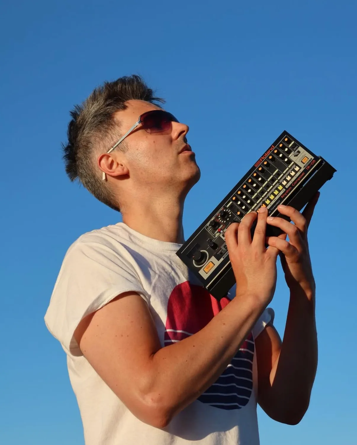 Phil holding a Roland TR-08 drum machine against an open sky